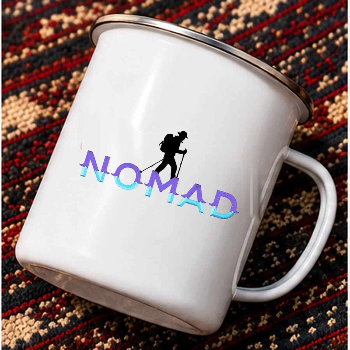Nomad enamel mug tilted on patterned travel rug showing the original mountain hiker graphic and purple cyan letters