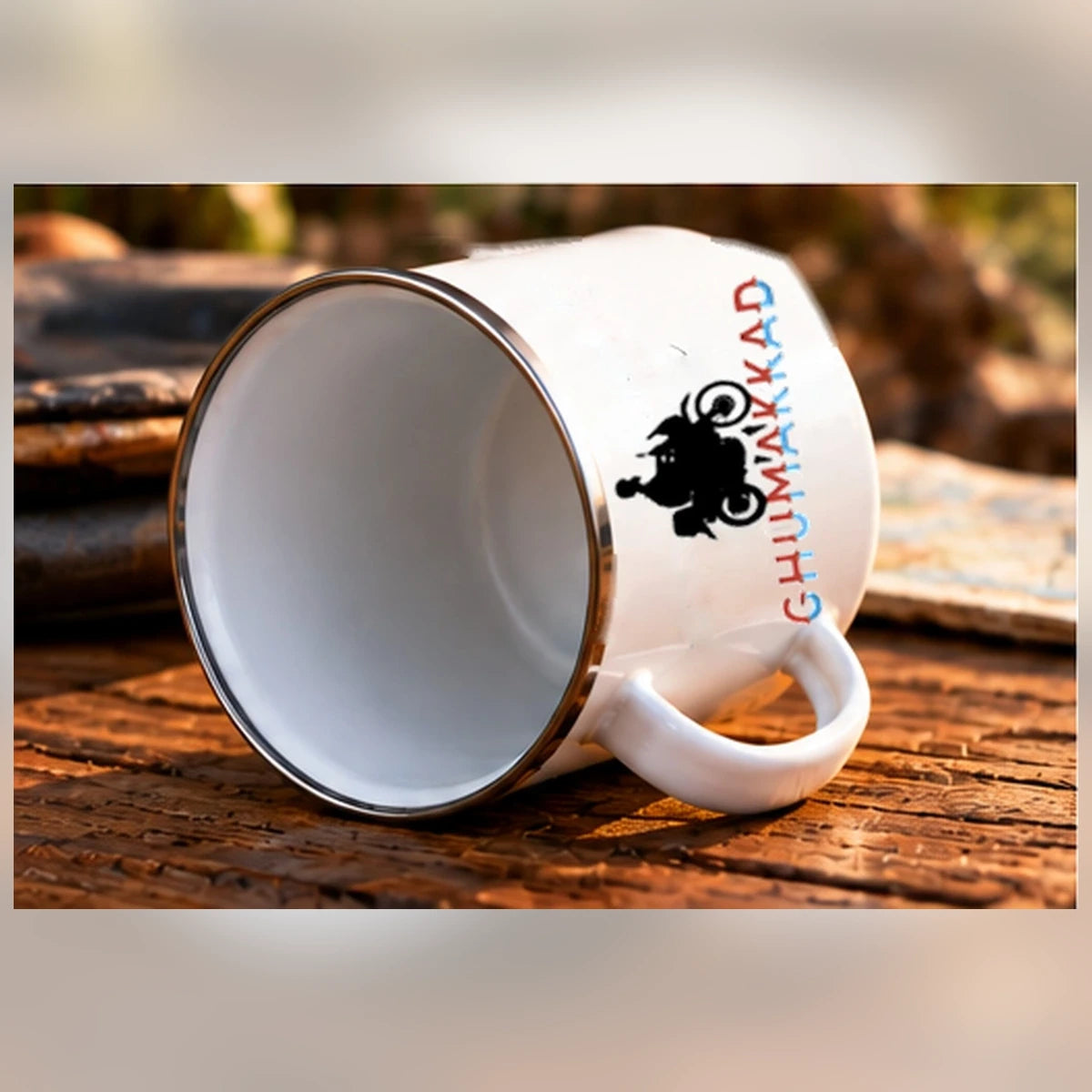 GHUMAKKAD enamel mug lying sideways on a wooden cafe table, with the corrected motorcycle artwork orientation