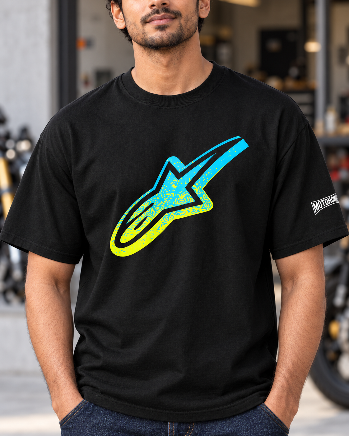 Close-up of the cyan and yellow speckled Astar print and Motohomies sleeve branding on the black T-shirt