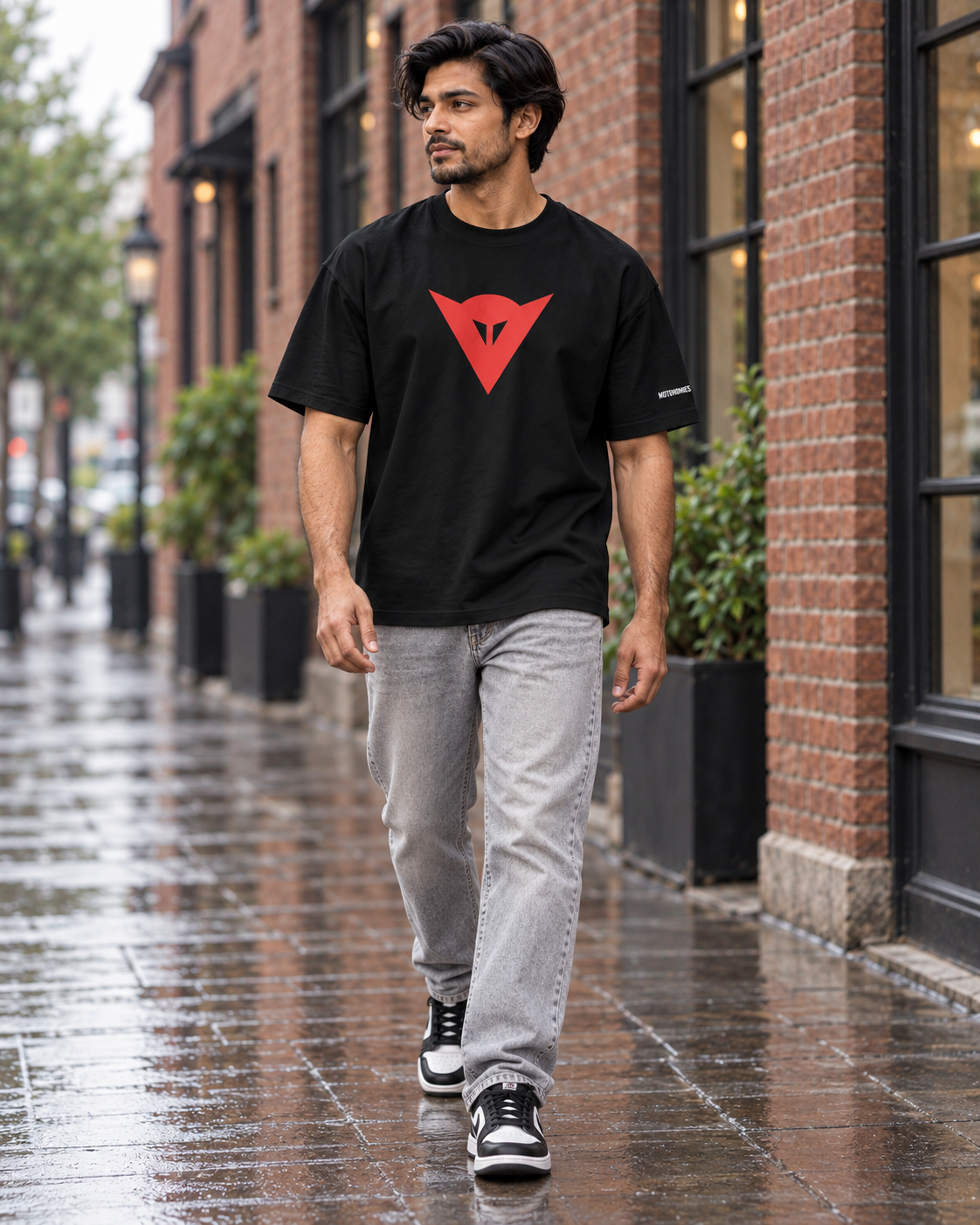 Model wearing the black Dainese logo T-shirt with grey jeans on a red-brick street