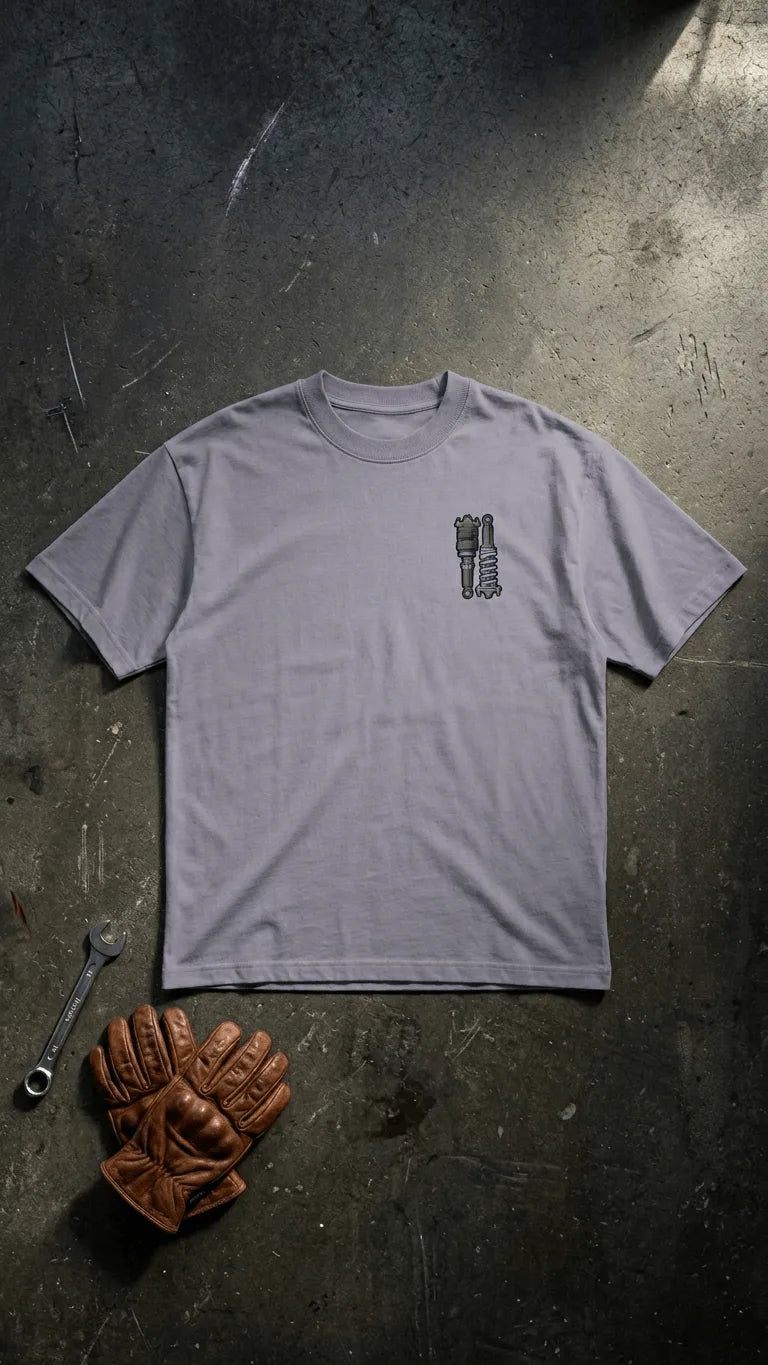 Stance Outlaws coilover tee back view with bold suspension graphic in grey, surrounded by mechanic tools and riding gloves