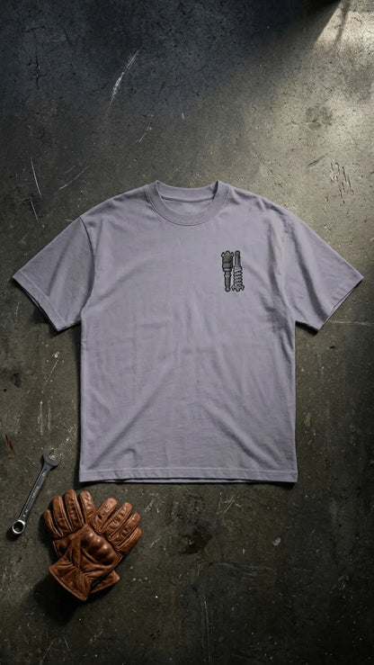 Stance Outlaws coilover tee back view with bold suspension graphic in grey, surrounded by mechanic tools and riding gloves