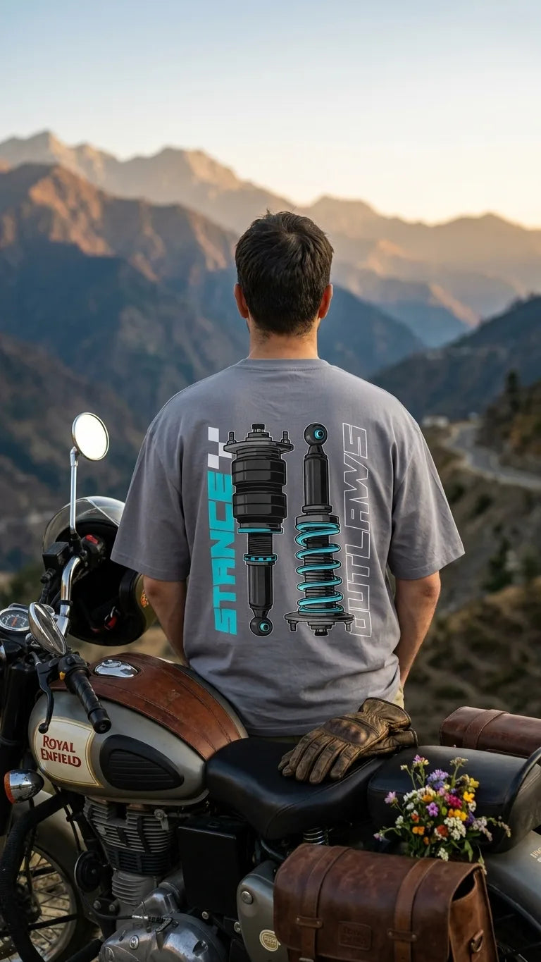 Rider in Stance Outlaws coilover tee on Royal Enfield motorcycle with Himalayan mountain range and winding road backdrop